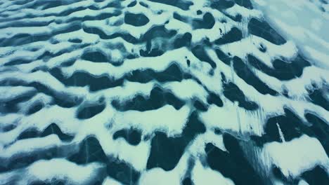 TOP-DOWN-aerial-shot-flying-backwards-over-the-wind-swept-patterns-of-snow-on-a-frozen-lake