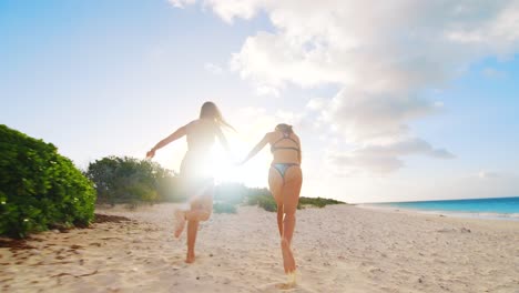Two-young-girls-in-bikinis-running-along-a-beautiful-sandy-beach-in-Bonaire,-Caribbean,-during-sunset