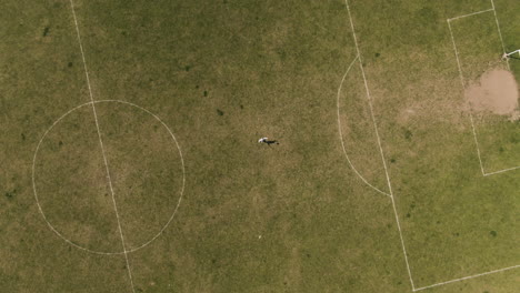 Single-player-practice-in-middle-of-local-football-field,-aerial-ascend-top-down-view