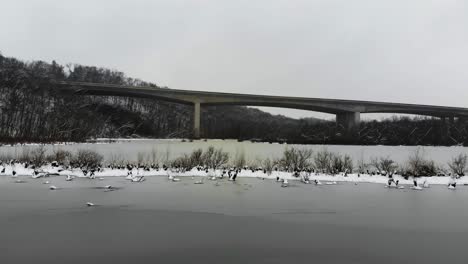 Eine-Niedrige-Luftaufnahme-über-Einem-Zugefrorenen-See-In-Richtung-Page-Brücke-Inmitten-Von-Fallendem-Schnee