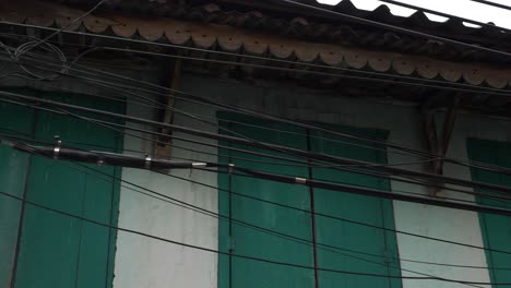 Panning-shot-of-messy-wiring-system-in-rural-village-against-white-building-with-green-shutters