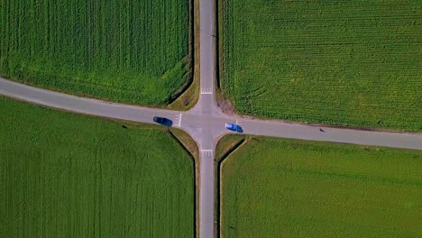 bird-eye-view-of-a-perfect-symmetrical-crossroad-with-green-fields-and-2-cars-passing