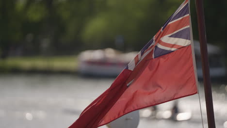 Red-Ensign-UK-flag-waving-in-light-breeze-on-sunny-day-with-water-in-background