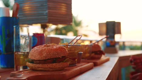 Persona-Comiendo-Hamburguesas-Y-Papas-Fritas-En-Un-Restaurante-Al-Aire-Libre-Durante-La-Puesta-De-Sol-En-El-Caribe