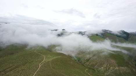 Aerial-panning-shot-across-open-green-mountain-ranges-as-cloud-cover-passes-low-to-ground