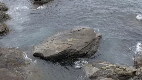 Flowing-ocean-waters-over-large-rock-boulders-on-coastal-shoreline