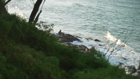 Headland-View-Of-Tradesman-Sitting-On-Rock-At-Beach-With-Ocean-Waves-Crashing,-4K