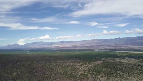 Vista-Aérea-Escénica-De-Un-Valle-Verde-Desierto-Y-Cadenas-Montañosas-En-Un-Día-Soleado