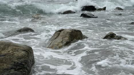 Low-angle-view-across-stones-poking-out-from-ocean-waves-on-rocky-shoreline