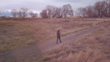 Man-walking-along-a-trail-in-a-cold,-wintery-field