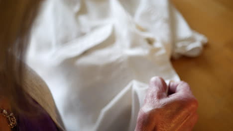 The-wrinkled-hands-of-an-aging-elderly-woman-repairing-a-button-on-a-white-dress-shirt-by-hand-with-thread-and-a-sewing-needle