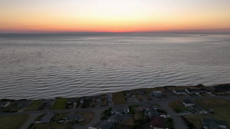 Aerial-view-pulling-away-from-the-orange-glow-of-the-sunset-to-reveal-a-beachfront-community