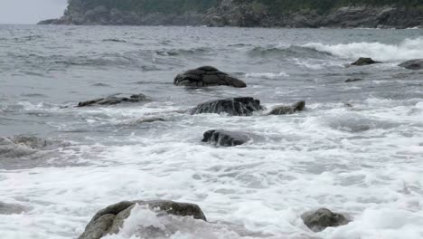 View-across-coastal-waters-as-waves-crash-over-rocks-poking-through-flowing-ocean-movement
