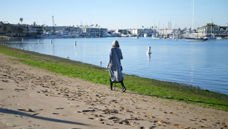 Una-Anciana-Saludable-Con-Un-Bastón-Para-Caminar-Por-Su-Discapacidad-Haciendo-Ejercicio-Y-Disfrutando-De-La-Playa-En-Cámara-Lenta-De-Newport,-California