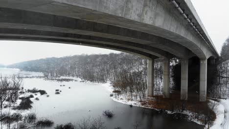 Drone-shot-flying-under-a-bridge-in-Missouri-over-a-frozen-lake-in-a-snowstorm