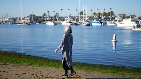 An-active-and-healthy-woman-at-retirement-age-with-a-walking-stick-for-her-disability-waving-to-friends-on-the-beach-in-Newport,-California-on-a-sunny-pleasant-day