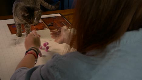 Woman-Rolls-Pink-RPG-Dice-on-Game-Table-Near-Pet-Cat