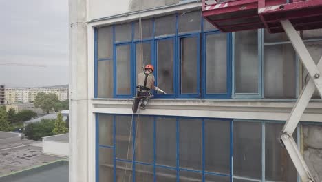 Panning-aerial-shot-across-industrial-climber-next-to-scissor-lift-scaffold-working-on-sealing-windows