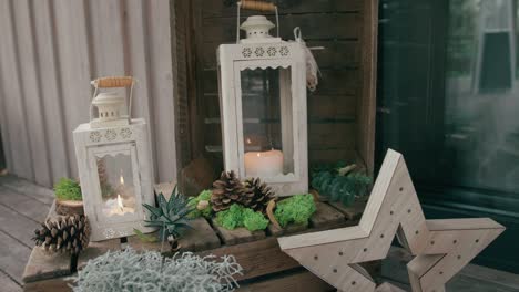 Decorations-made-with-candles-inside-white-lanterns,-small-plants-and-pinecones,-on-a-wooden-surface