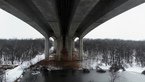 A-drone-flight-between-columns-of-Pace-Bridge-in-Missouri,-over-a-snowy-lake