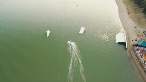 Drone-shot-of-a-person-wake-boarding-on-the-lake-Zlate-Piesky,-Bratislava,-Slovakia,-near-the-shore