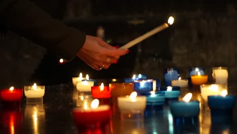 Shot-of-the-hand-of-a-young-woman-praying,-lighting-a-candle-in-a-Catholic-Church