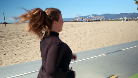 Focused-fit-woman-jogging-on-the-pathway-of-beach-Santa-Monica-California-on-a-harsh-sunny-morning