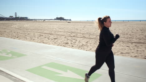 Determined-young-woman-jogging-on-the-pathway-of-the-sandy-beach-of-Santa-Monica-California