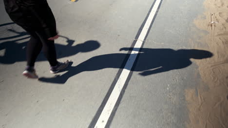 Woman-taking-a-stroll-on-the-beach-road,-with-focus-on-the-shadow-at-Santa-Monica