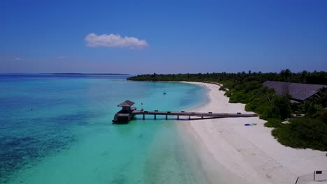 Maldives-secluded-beach,-aerial-forward-push-towards-wooden-jetty-4k