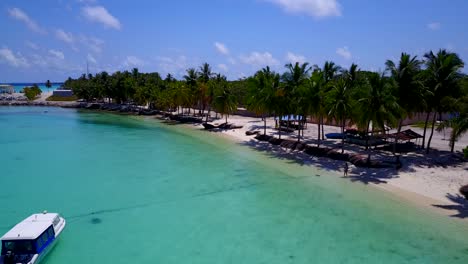 aerial-footage-along-the-coast-of-a-tropical-island-with-palm-trees-on-the-white-sandy-beaches-and-a-touristic-boat-anchored