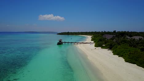 Eine-Horizontale-Luftaufnahme-Eines-Resorthotels-Und-Seiner-Holzterrasse-Am-Türkisfarbenen-Meer-Auf-Den-Malediven,-Drohnenaufnahmen-An-Einem-Klaren-Tag