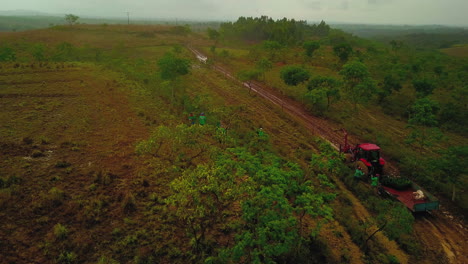 Aerial-shot-of-field-workers-planting-coyol-palm-trees-from-a-trailer-attached-to-a-tractor,-palm-oil-producing-farm