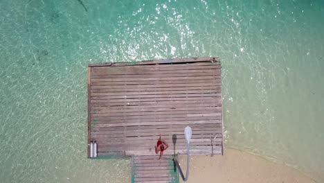 Mann-Läuft-Auf-Steg-Und-Taucht-Dann-In-Wunderschöne-Maledivengewässer,-Von-Oben-Nach-Unten-Luft-4k