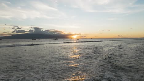 Sun-sets-behind-Lanai-Island-and-anchored-boats-as-surfer-whips-on-Lahaina-waves