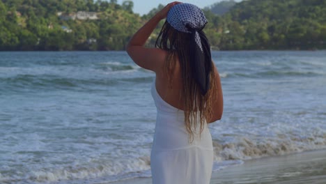 Eine-Junge-Dame-In-Einem-Weißen-Strandkleid-Blickt-Im-Hintergrund-Auf-Die-Meereswellen