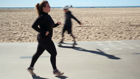 Young-fit-woman-jogging-on-the-cycle-lane-of-the-sandy-beach-of-Santa-Monica-California,-on-a-bright-sunny-day