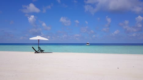 a-slow-slider-move-on-the-white-beaches-of-the-turquoise-Caribbean-sea,-with-two-empty-wooden-seats-under-a-white-parasol