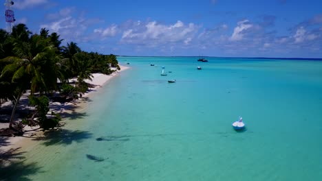 aerial-footage-along-the-coast-of-a-tropical-island-with-palm-trees-on-the-white-sandy-beaches-and-small-boats-anchored-by-the-shoreline