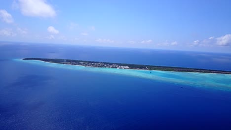 high-altitude-aerial-view-of-an-island-covered-with-palm-trees-in-the-Maldives-as-the-color-of-the-sea-goes-from-turquoise-to-dark-blue