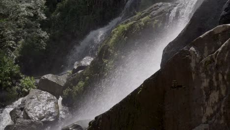 Aguas-En-Cascada-Que-Se-Estrellan-Sobre-Un-Terreno-Montañoso-Rocoso-Y-Empinado-Con-Bosques-En-La-Vista-De-Fondo