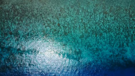 Aerial-orbit-above-shot-of-beautiful-clear-waters-showing-coral-and-shimmers-from-sun