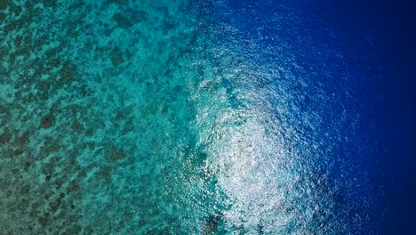 Shallow-to-deep-blue-water-on-reef-fall-off-into-depths,-birds-eyes-view-rotating-shot