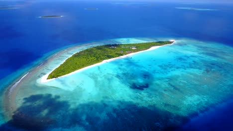 high-altitude-aerial-view-of-an-island-covered-with-palm-trees-in-the-Maldives-as-the-color-of-the-sea-goes-from-turquoise-to-dark-blue