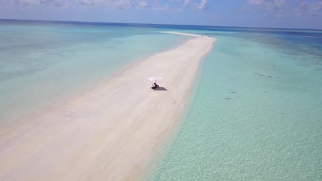 Man-resting-under-umbrella-on-deserted-sand-spit-island-in-the-middle-of-Indian-ocean,-Slow-aerial-pan-4k