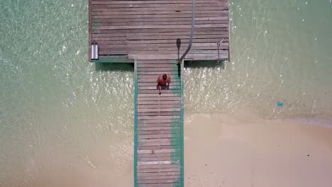 Man-runs-into-frame-and-across-pier-then-dives-into-bright-blue-waters-on-tropical-island