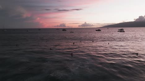 Surfers-and-boaters-enjoying-ocean-view-of-red-pink-sunset,-Lahaina-Maui-Hawaii