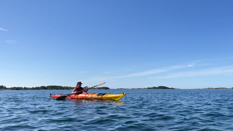 Girl-paddling-on-a-bright-orange-kayak-in-open-water-with-islands-in-the-background-on-a-sunny-day