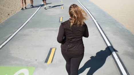 Focused-young-woman-running-in-a-mid-pace-on-the-pathway-of-Santa-Monica-beach