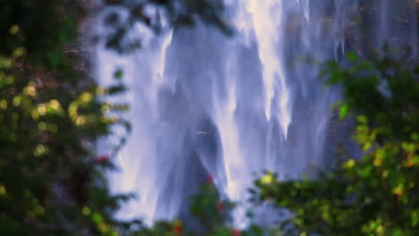 Close-up-footage-of-at-a-misty-waterfall-surrounded-by-green-lush-branches-and-trees